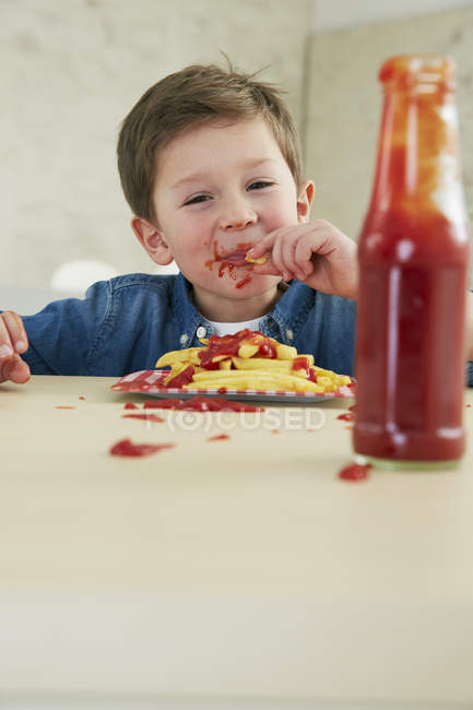 Boy eating French fries with ketchup — Stock Photo