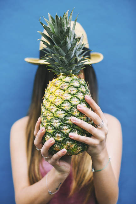 Donna che tiene ananas davanti al viso su sfondo blu — Foto stock