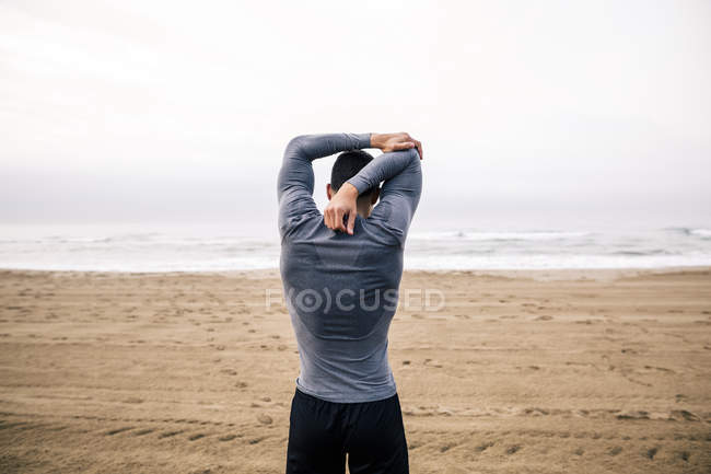 Jeune homme sportif étirant sur la plage — Photo de stock