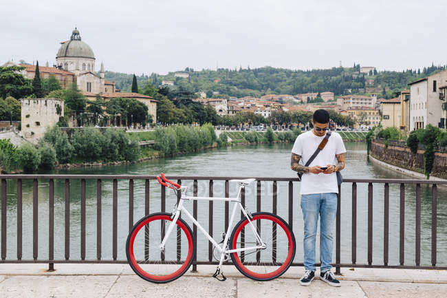 Italy, Verona, young man with a bicycle standing on a bridge — Stock Photo