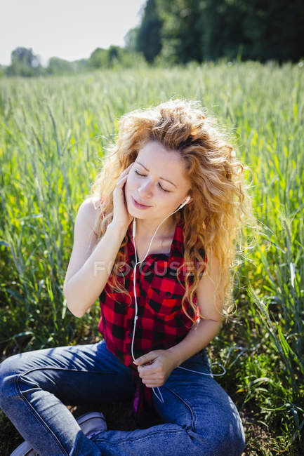 Ritratto di donna seduta in un campo a sentire musica con auricolari — Foto stock