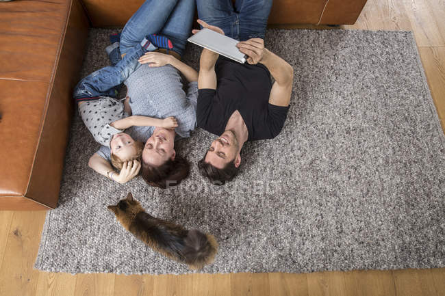 Familia feliz acostada en el suelo, usando tableta digital - foto de stock