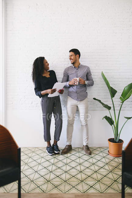 Dos jóvenes empresarios de pie contra la pared con papeles y una taza de café - foto de stock