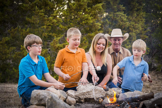 Familia Asando malvaviscos sobre fuego de campamento - foto de stock