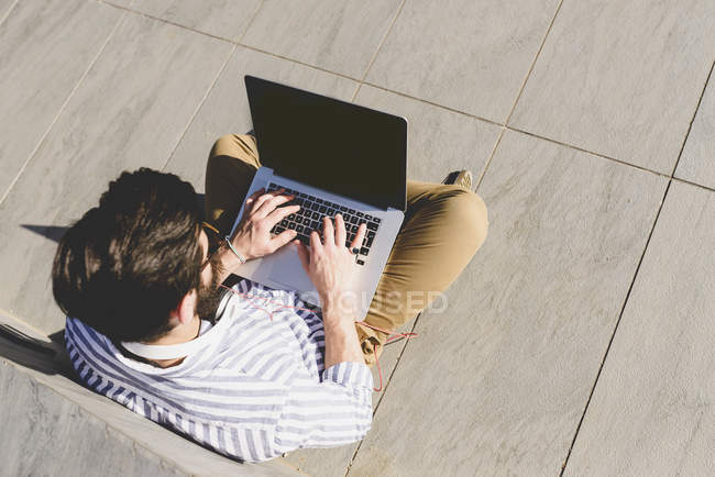 Человек сидит на земле и с помощью ноутбука — стоковое фото