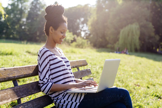 Junge Frau sitzt mit Laptop auf Parkbank — Stockfoto