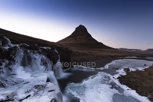 Islanda, penisola di Snaefellsnes, Grundafjoerdur, Kirkjufell, cascata di ghiaccio e silhouette di montagna sullo sfondo — Foto stock