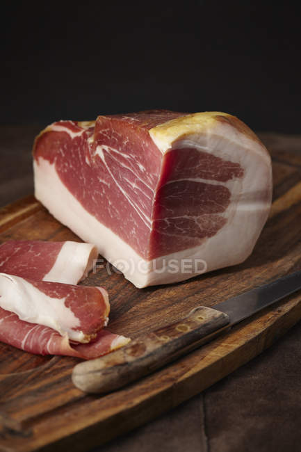 Prosciutto di Parma parzialmente affettato su tagliere di legno con coltello — Foto stock