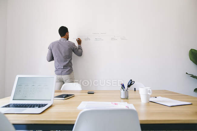 Mann schreibt Diagramm an Wand im modernen Büro — Stockfoto