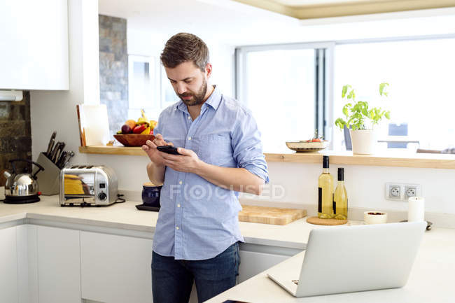 Hombre trabajando en la cocina usando el teléfono inteligente - foto de stock
