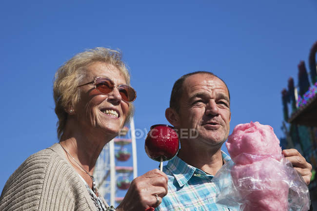 Homem e mulher na feira desfrutando doces de maçã e algodão cristalizados — Fotografia de Stock