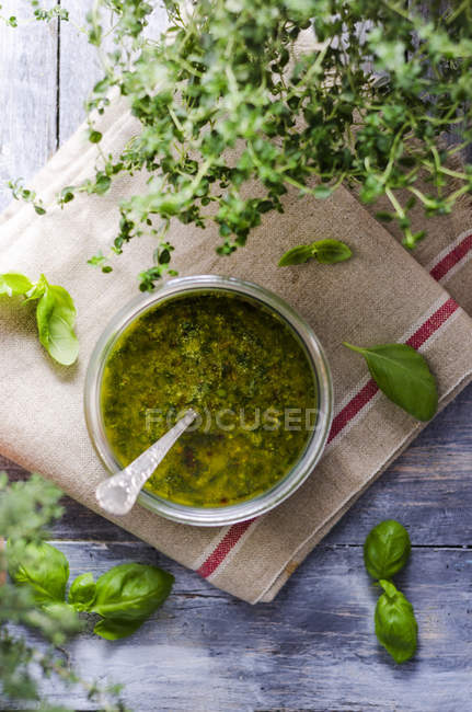 Basil pesto in a glass and fresh green leaves on kitchen towel, top view — Stock Photo