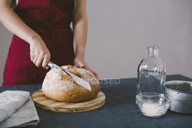 Donna che taglia pane fresco fatto in casa su tavola di legno — Foto stock