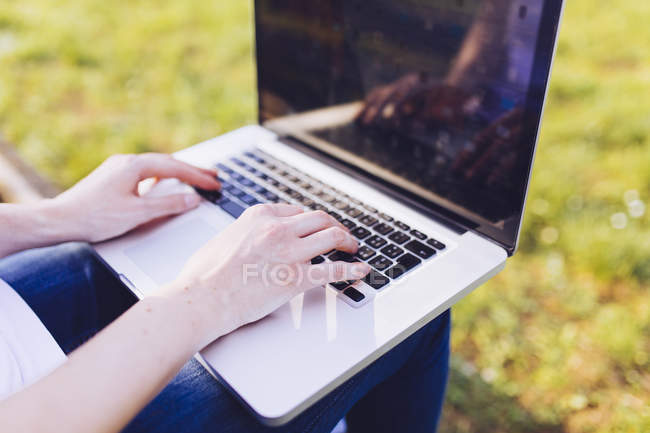 Жінка навчається в ноутбуці, сидячи на лавці в парку — стокове фото