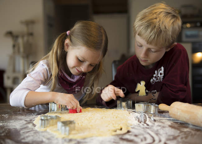 Junge und Mädchen schneiden Kekse mit Ausstecher aus — Stockfoto
