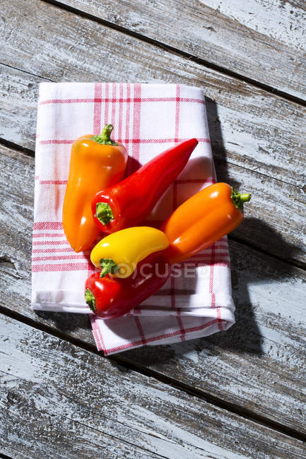 Peperoni rossi, arancioni e gialli su tovagliolo da cucina su tavolo di legno — Foto stock