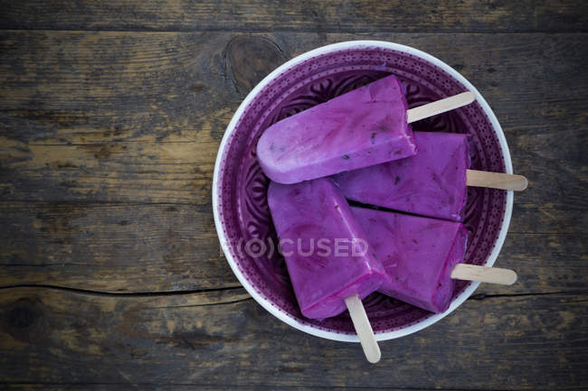 Elevated view of plate of four yogurt blueberry ice lollies on wooden table — Stock Photo