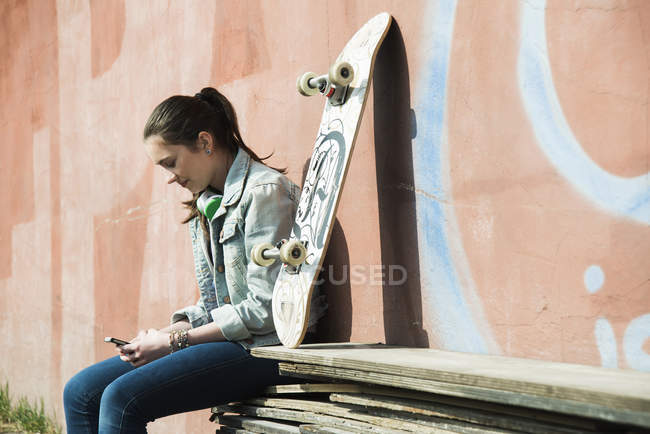 Девушка-подросток со скейтбордом на смартфоне — стоковое фото