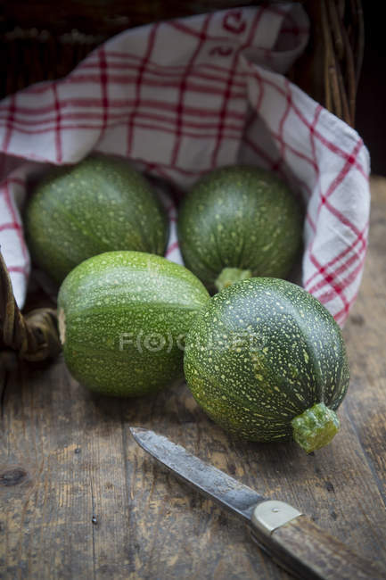 Cuatro calabacines redondos con toalla de cocina y cuchillo sobre mesa de madera oscura - foto de stock