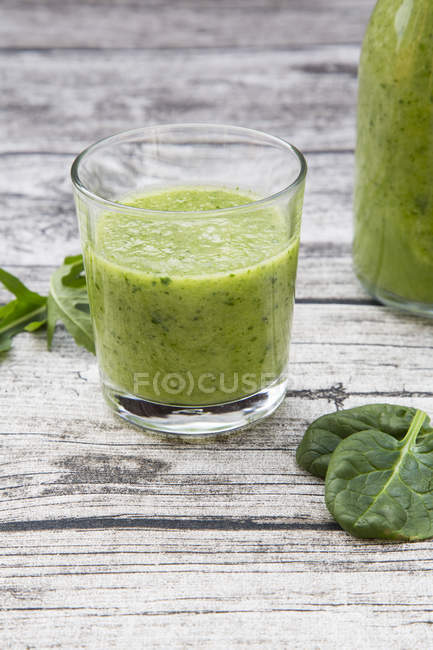Glass of green fruit smoothie with spinach, rocket salad and on grey wooden table — Stock Photo