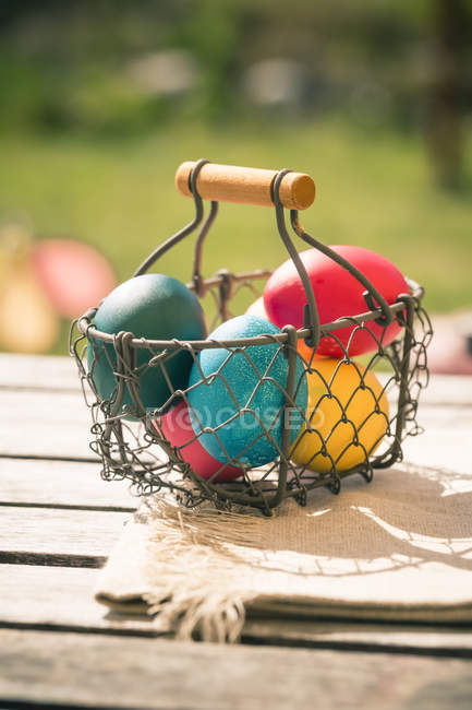 Close-up de cesta de ferro com ovos de Páscoa coloridos na mesa de madeira — Fotografia de Stock
