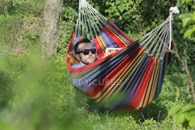 Young man lying in hammock and reading a magazine — Stock Photo