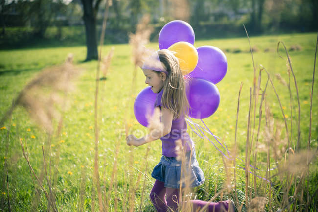 Menina com balões correndo em um prado — Fotografia de Stock