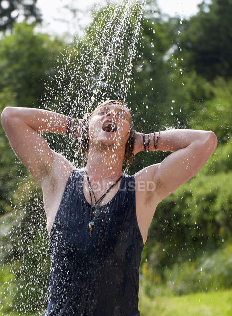 Молода людина, приймаючи душ в саду — стокове фото