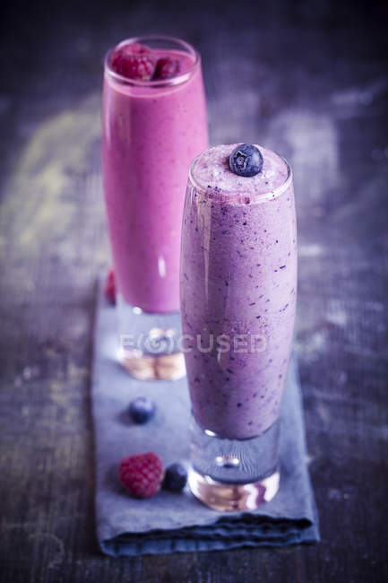 Glasses of fruit smoothies on napkin on wooden surface — Stock Photo