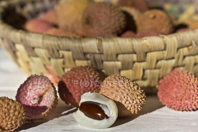 Peeled and whole fresh lychees with basket on background — Stock Photo