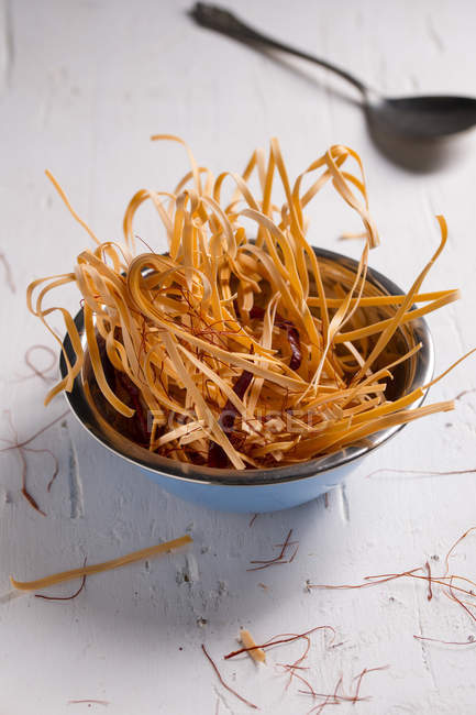 Bowl of uncooked chili pasta with chili pods and chili threads on white wooden table — Stock Photo