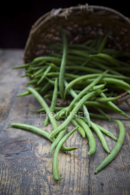 Green beans and upturned basket on dark wood — Stock Photo