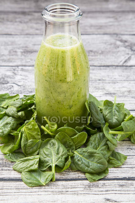 Bottiglia di frullato verde con spinaci e insalata di rucola su tavolo di legno grigio con foglie di spinaci freschi — Foto stock