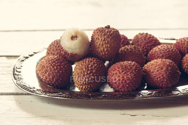 Silver plate of whole lychees with half on wooden table — Stock Photo