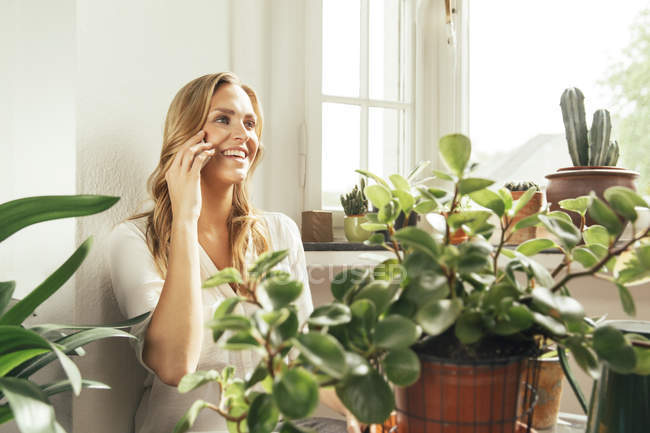 Усміхається жінка вдома навколо рослин горщиків — стокове фото