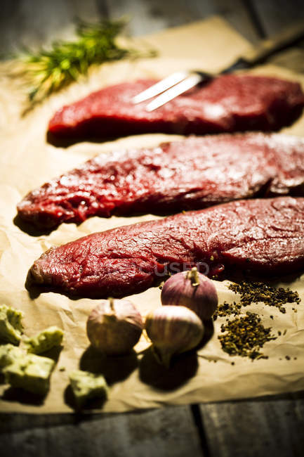 Biftecks de boeuf, ail, romarin, beurre d'herbes et poivre sur papier sulfurisé — Photo de stock