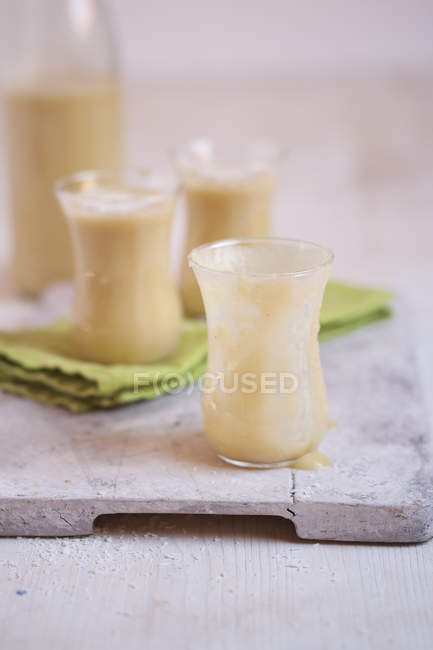 Lunettes de smoothie à la mangue avec noix de coco desséchée sur tissu sur planche de bois — Photo de stock