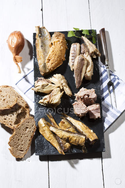 Variety of pickled and marinated fish on slate on white wooden table with bread — Stock Photo