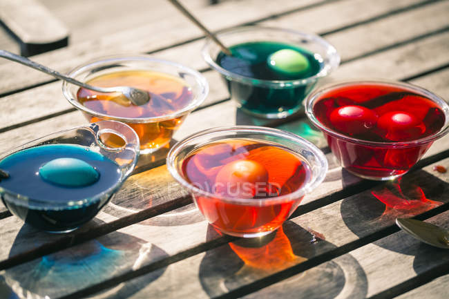 Close-up of colorful Easter eggs in glass bowls with dyes on wooden table — Stock Photo