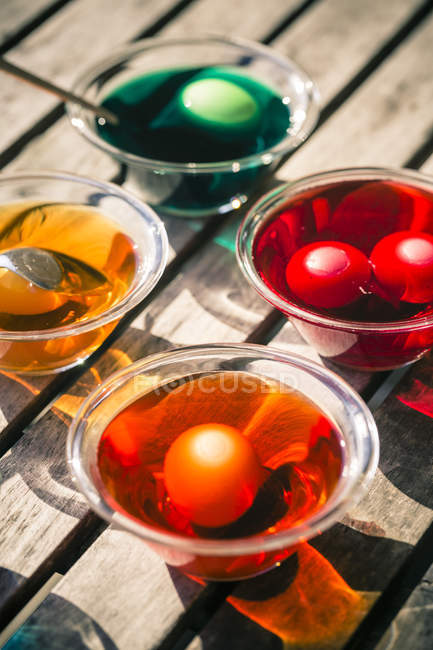 Підвищені подання барвисті великодні яйця в скляних миски з барвники на дерев'яні таблиці — стокове фото