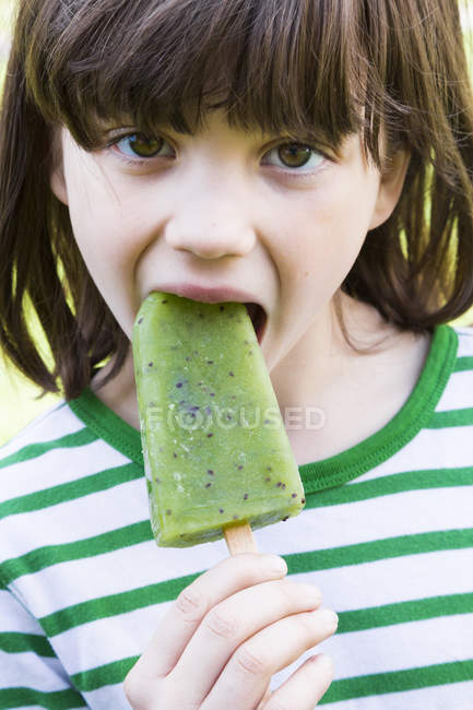 Close-up of girl eating kiwi ice lolly — Stock Photo