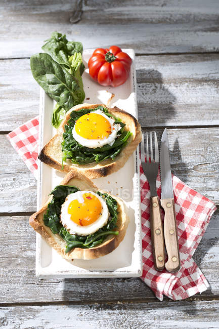 Fried eggs and spinach on toast with tomatoes — Stock Photo