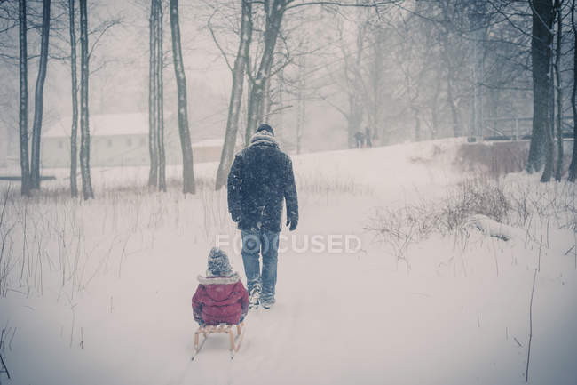 Padre tirando de trineo con hijo en la nieve - foto de stock