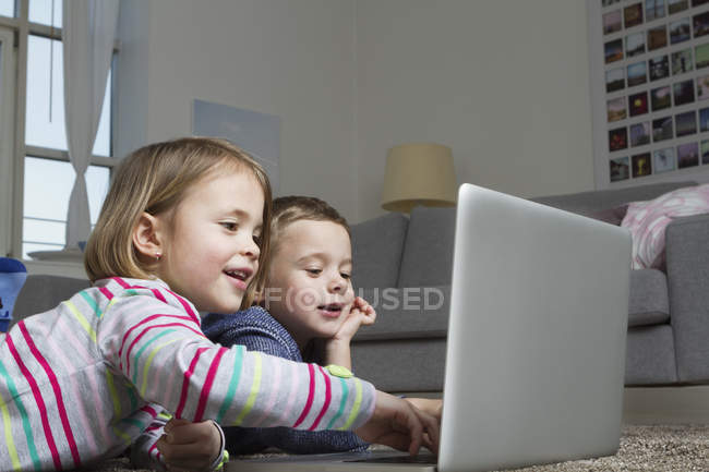 Brother and sister using laptop on carpet in living room — Stock Photo