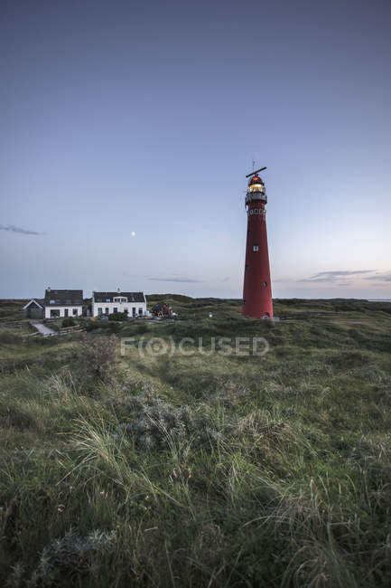 Paesi Bassi, faro illuminato con edifici al tramonto — Foto stock