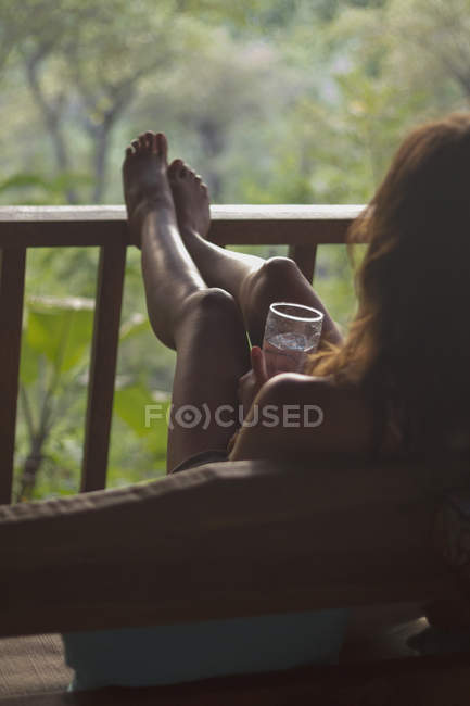Молода жінка, сидячи на дивані з водою скло в веранді — стокове фото