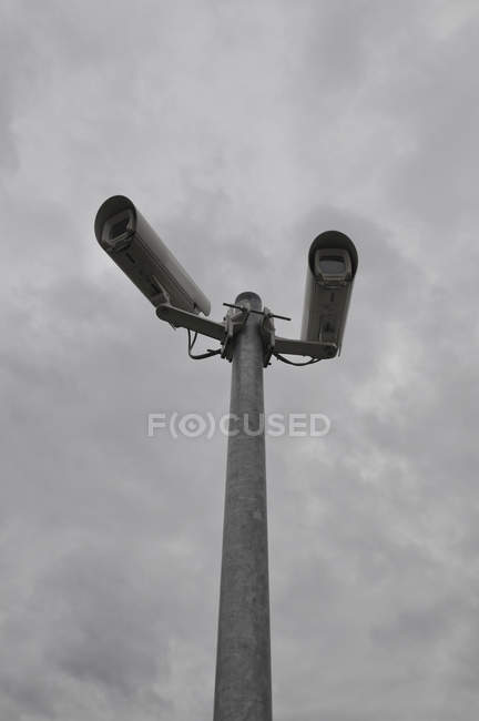 Vista basso angolo di telecamere di osservazione su palo metallico contro cielo nuvoloso — Foto stock