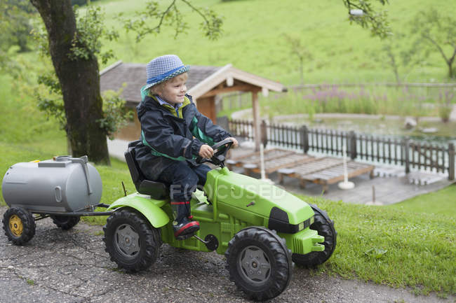 Ragazzo seduto in trattore giocattolo con rimorchio — Foto stock