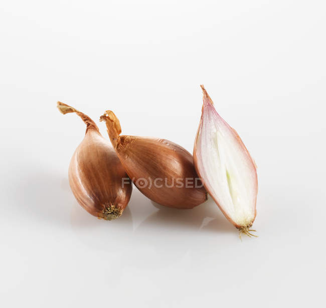 Ganze und halbierte frische Schalotten auf weißem Hintergrund — Stockfoto