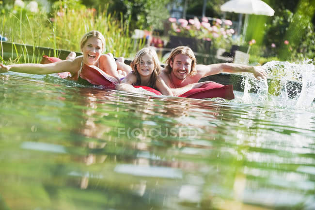 Familia flotando en el aire acondicionado en la piscina natural - foto de stock
